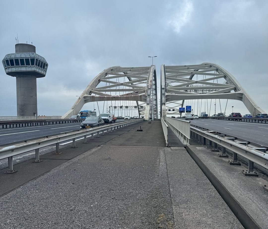 Een stalen boogbrug over de snelweg met een verkeerstoren