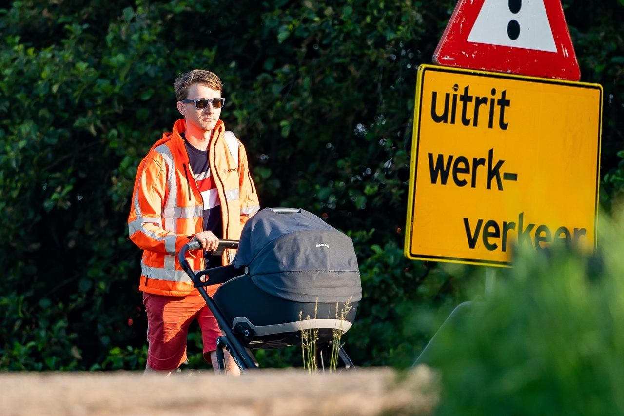 Ben in oranje werkkleding met de kinderwagen langs een bord 'uitrit werkverkeer'